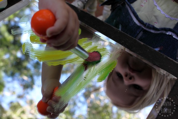 Toddler painting reflected leaves on a mirror